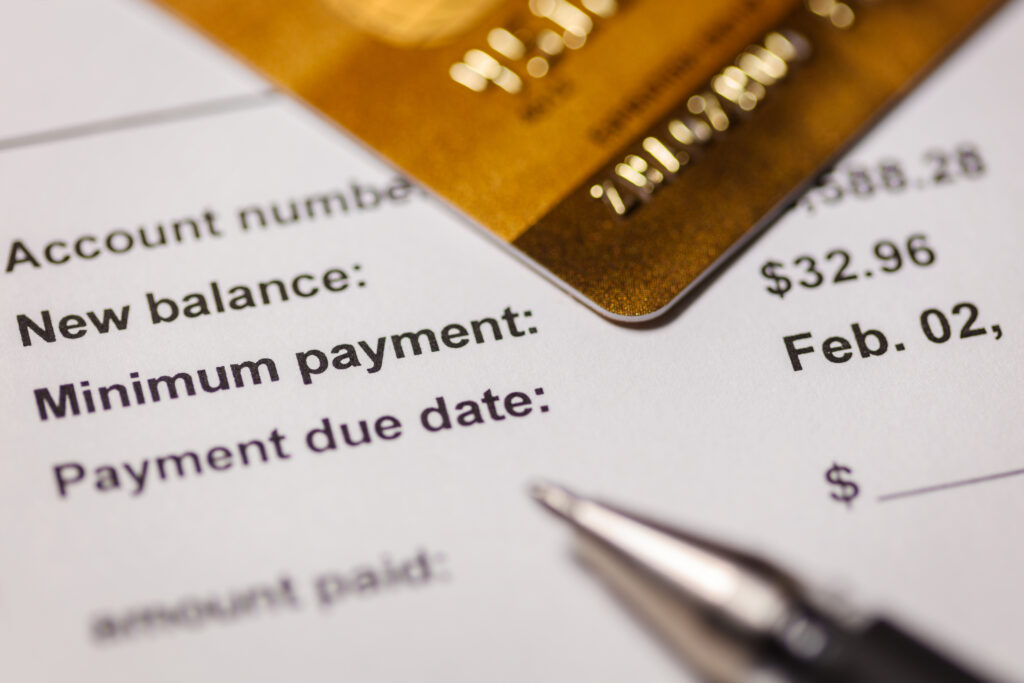 Close-up of a credit card resting on a billing statement showing a new balance, minimum payment, and due date.