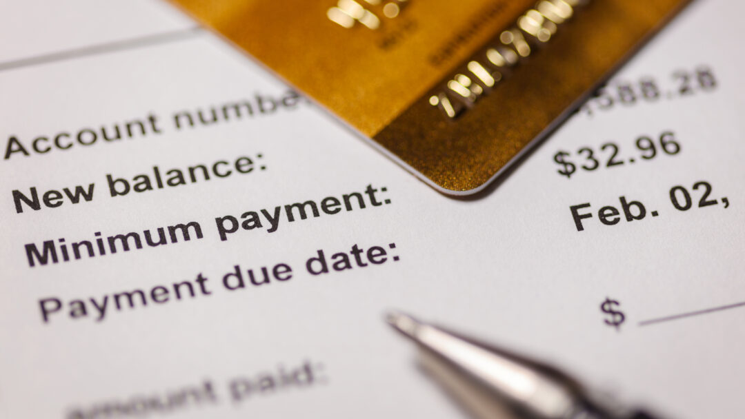 Close-up of a credit card resting on a billing statement showing a new balance, minimum payment, and due date.