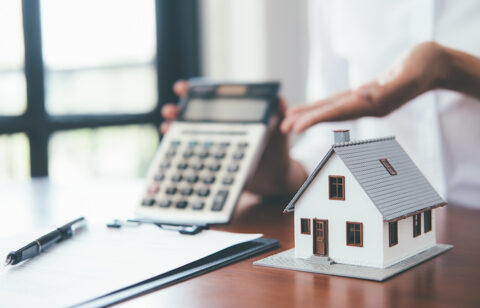 Small model house on a desk with a calculator and paperwork in the background.