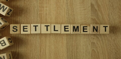 Wooden letter tiles spelling “SETTLEMENT” arranged on a wood surface.