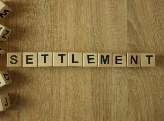 Wooden letter tiles spelling “SETTLEMENT” arranged on a wood surface.