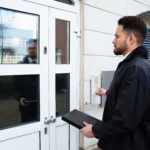 Person standing at a door and using an entry buzzer, carrying a document case.