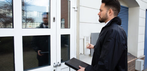 Person standing at a door and using an entry buzzer, carrying a document case.