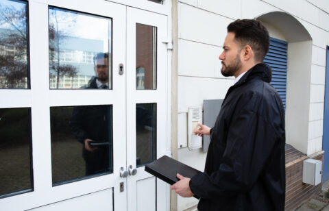 Person standing at a door and using an entry buzzer, carrying a document case.