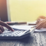 Close-up of hands using a calculator while reviewing paperwork on a desk.