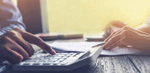 Close-up of hands using a calculator while reviewing paperwork on a desk.
