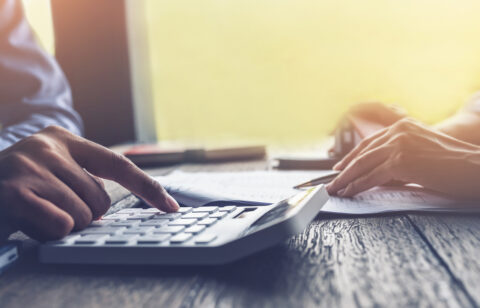 Close-up of hands using a calculator while reviewing paperwork on a desk.