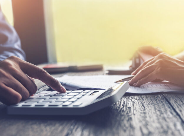 Close-up of hands using a calculator while reviewing paperwork on a desk.