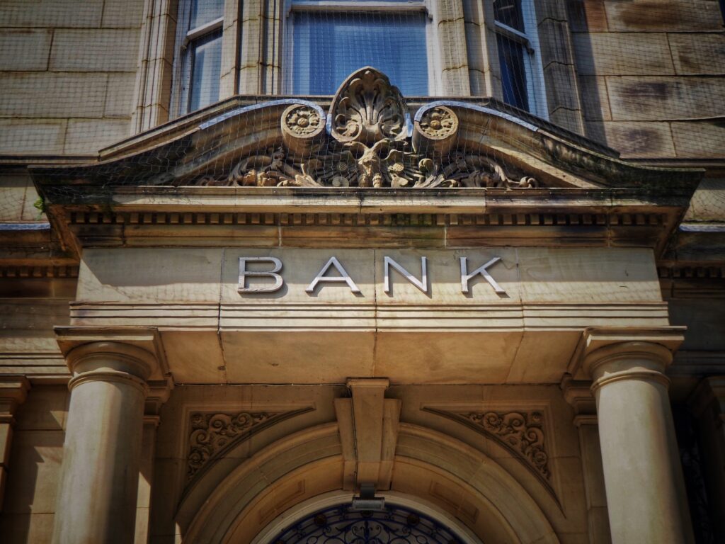 Stone bank building facade with columns and the word “BANK” displayed above the entrance.