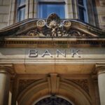 Stone bank building facade with columns and the word “BANK” displayed above the entrance.