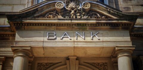 Stone bank building facade with columns and the word “BANK” displayed above the entrance.