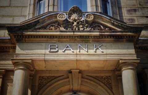 Stone bank building facade with columns and the word “BANK” displayed above the entrance.