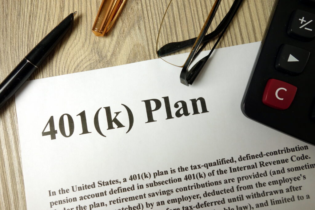 Document labeled “401(k) Plan” on a desk with a pen, eyeglasses, and calculator nearby.