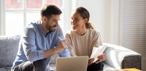Couple sitting on a couch reviewing bills and using a laptop together.