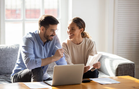Couple sitting on a couch reviewing bills and using a laptop together.