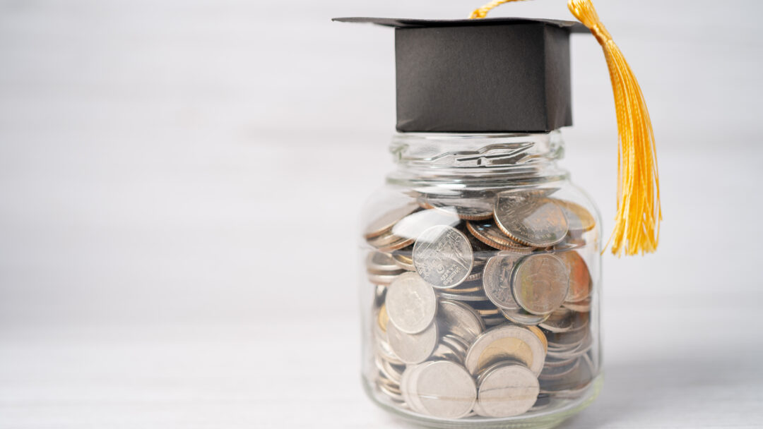 Jar of mixed coins with a black graduation cap and tassel on top