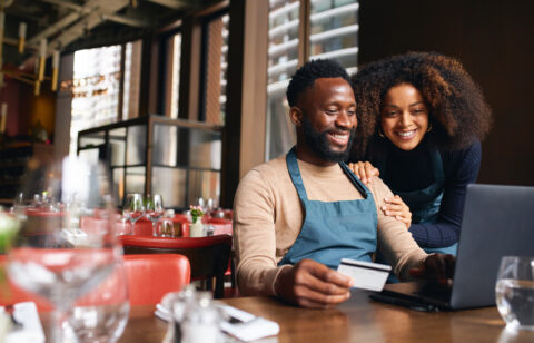 Pair of small business workers reviewing something online with a laptop and credit card inside a dining area.