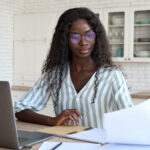 Woman reviewing a document at a table with a laptop and notebook nearby.