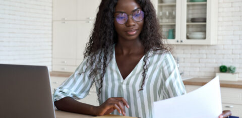 Woman reviewing a document at a table with a laptop and notebook nearby.