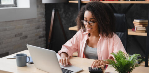 Woman working at a desk with a laptop and calculator, managing finances in a home office.