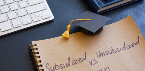 Notebook with the words “Subsidized vs Unsubsidized Loan” written on it, next to a graduation cap and keyboard.