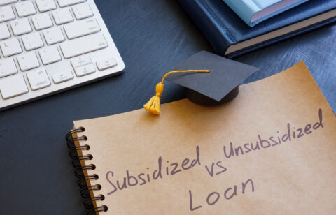 Notebook with the words “Subsidized vs Unsubsidized Loan” written on it, next to a graduation cap and keyboard.