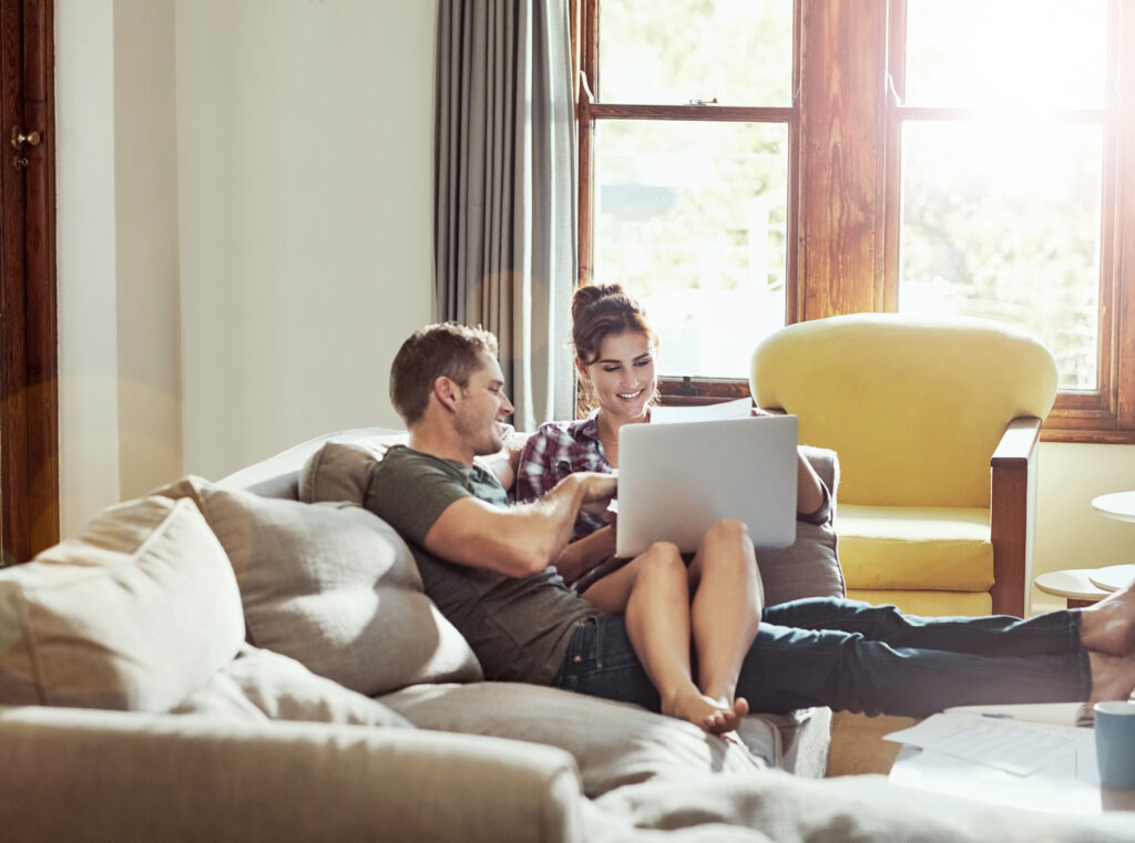 Couple relaxing on a couch at home, looking at a laptop together.