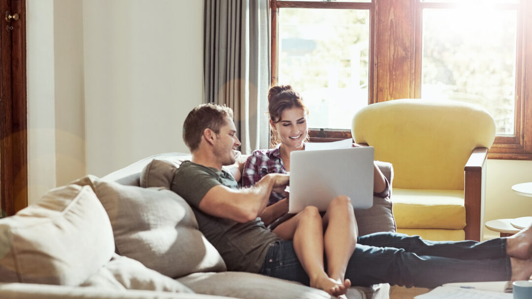Couple relaxing on a couch at home, looking at a laptop together.