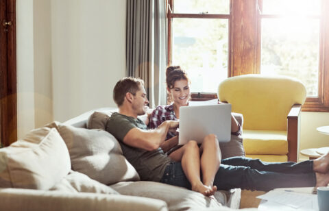 Couple relaxing on a couch at home, looking at a laptop together.