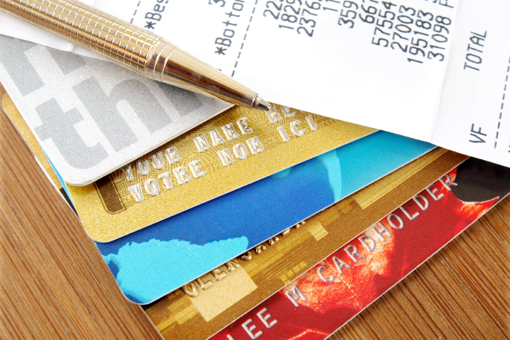 Stack of credit cards with a pen and a receipt showing charges and totals on a wooden surface.