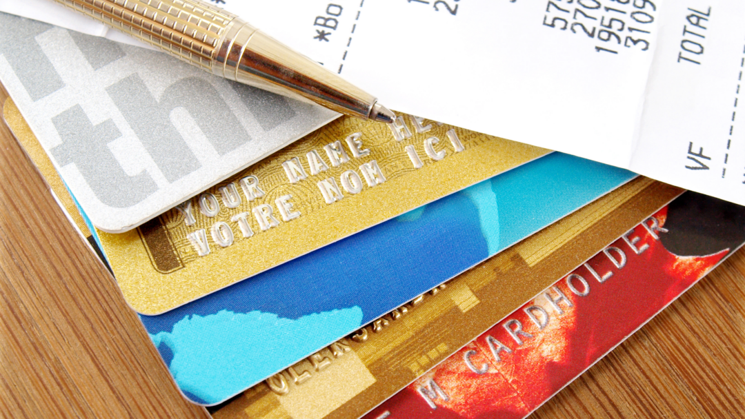 Stack of credit cards with a pen and a receipt showing charges and totals on a wooden surface.