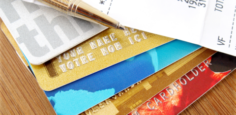 Stack of credit cards with a pen and a receipt showing charges and totals on a wooden surface.