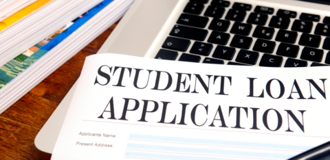 Student loan application form on a desk next to a laptop, pen, and stacked books