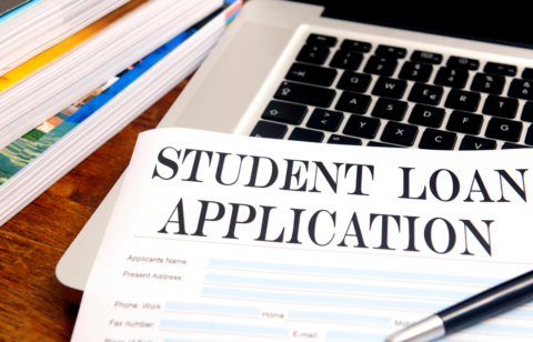 Student loan application form on a desk next to a laptop, pen, and stacked books