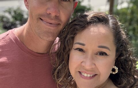 Smiling couple taking a close-up selfie outdoors with trees and sunlight in the background