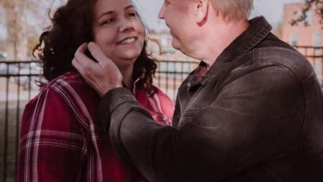 Man and woman sharing a warm moment outside, with the man holding the woman’s cheek as they smile at each other.