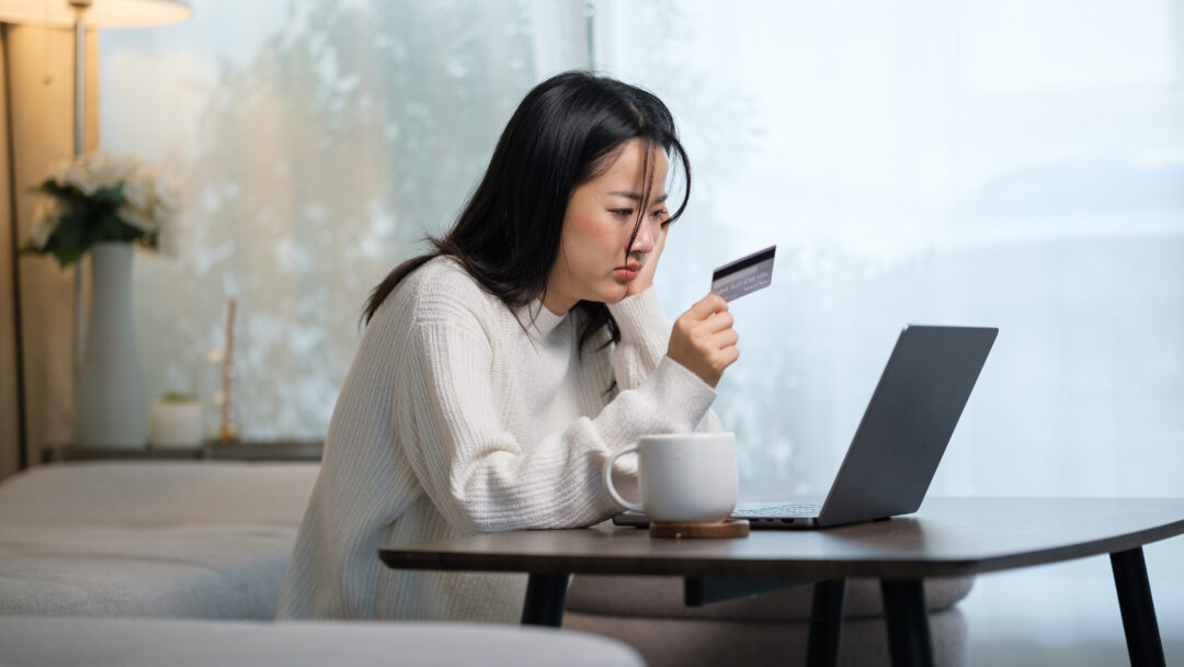 Person sitting at a table using a laptop while holding a credit card, appearing focused