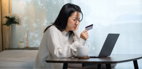 Person sitting at a table using a laptop while holding a credit card, appearing focused