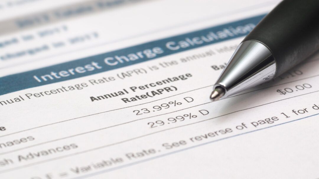 Credit card interest charges document displaying APR rates, with a pen pointing toward the listed percentages.