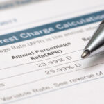 Credit card interest charges document displaying APR rates, with a pen pointing toward the listed percentages.