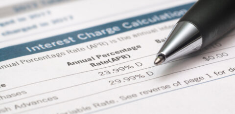 Credit card interest charges document displaying APR rates, with a pen pointing toward the listed percentages.