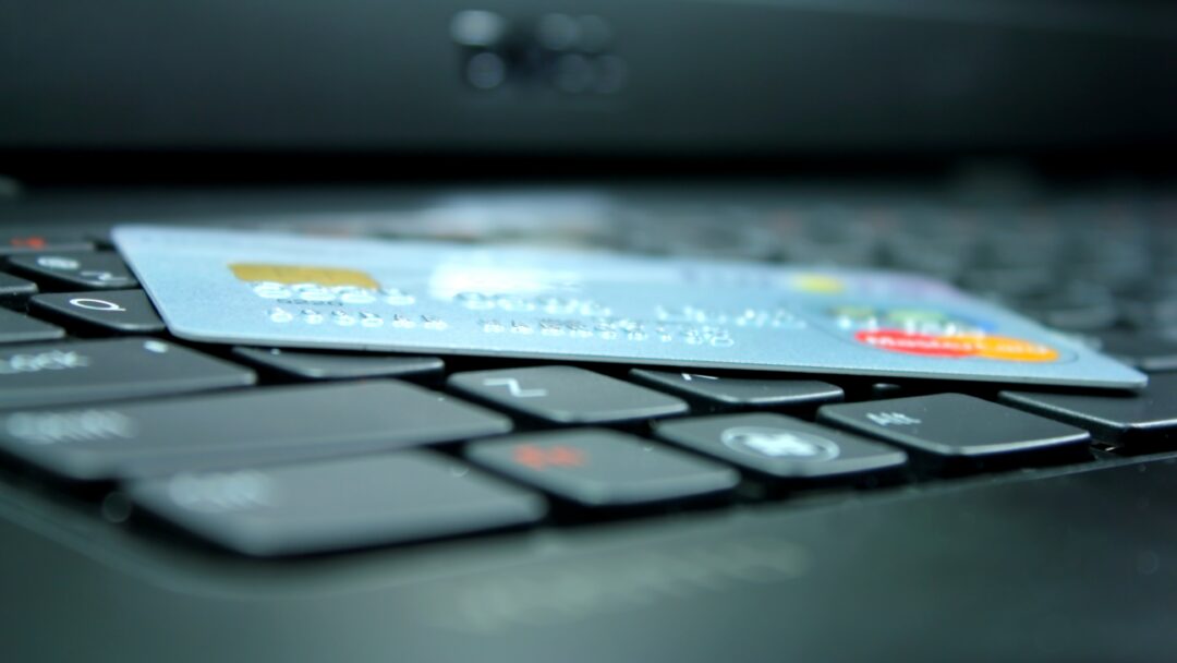 Credit card placed across computer keys, with a blurred laptop screen in the background.
