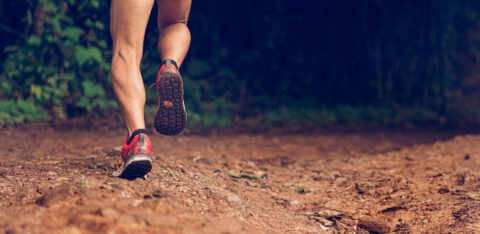 Runner’s legs in motion on a rugged path, moving through a wooded outdoor area