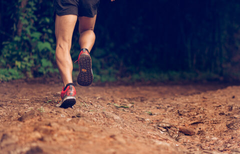 Runner’s legs in motion on a rugged path, moving through a wooded outdoor area