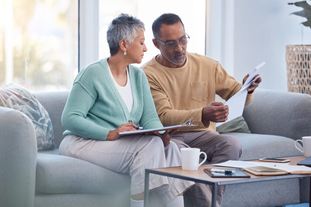 Older couple reviewing paperwork together on a couch, with one holding a document and the other taking notes