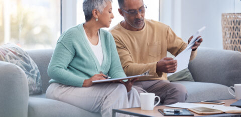 Older couple reviewing paperwork together on a couch, with one holding a document and the other taking notes