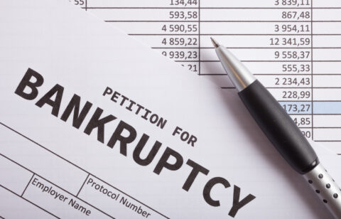Close-up of a document labeled “petition for bankruptcy” with a pen resting on financial statements