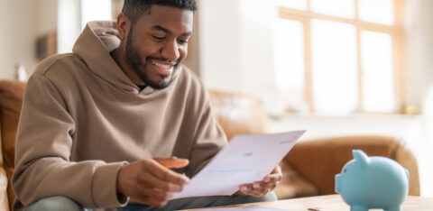 Person sitting at a table smiling while reviewing a document, with a piggy bank nearby