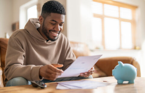 Person sitting at a table smiling while reviewing a document, with a piggy bank nearby