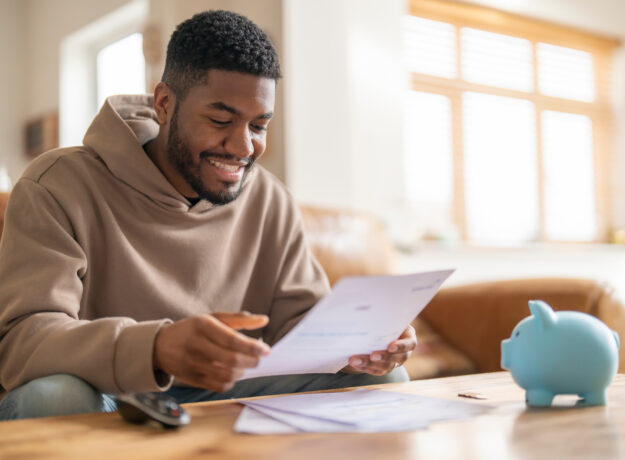 Person sitting at a table smiling while reviewing a document, with a piggy bank nearby